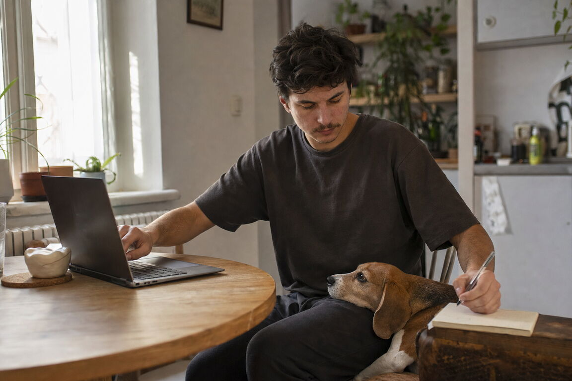 O proprietară de câine compară informații pe laptop, cu câinele întins liniștit lângă ea.